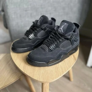 Nike Air Jordan 4 Retro Black Cat - Säljer ett par Nike Air Jordan 4 Retro Black Cat sneakers i helsvart mocka och syntet. Klassisk siluett med meshpaneler, snörning och ikoniska Jumpman-loggor på plös och sula. Riktigt clean och stilren modell som passar till allt. Har boxen tlll dom då dom e helt nya skickar dom över hela Sverige👍