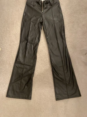 Svarta skinnbyxor - Säljer ett par svarta bootcut skinnbyxor med låg midja och dragkedja framtill. Säljer byxorna de de har blivit förkorta för mig och jag är 170cm. Byxorna är i storlek 158 men enligt mig tycker ja de passar om man är längre också, till 165 ungäfär.
