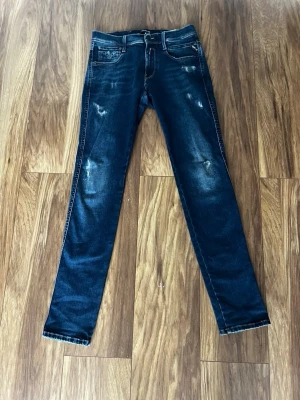 Replay anbass - Säljer ett par mörkblå jeans från Replay med snygga slitningar och klassiska kontrastsömmar. Modellen har tapered fit och normal midja. Materialet är mjukt jeans-tyg som sitter skönt. Bakfickorna har Replay-logga och coola detaljer.