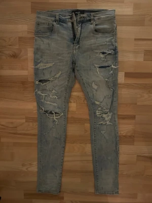 Ljusblå ripped skinny jeans från Amiri - Säljer ett par ljusblå skinny jeans från Amiri med rejält slitna och trasiga detaljer framtill. Jeansen har klassisk femficksdesign, låg midja och är tillverkade i stretchig bomull. Perfekta för dig som gillar en edgy och avslappnad stil.