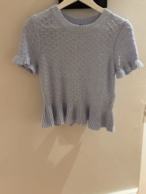 Ljusblå stickad topp med volang - Supersöt ljusblå stickad topp med korta ärmar och volangdetaljer vid ärmslut och nederkant. Användt 2 gånger och syns inte att den anväts❣️💕