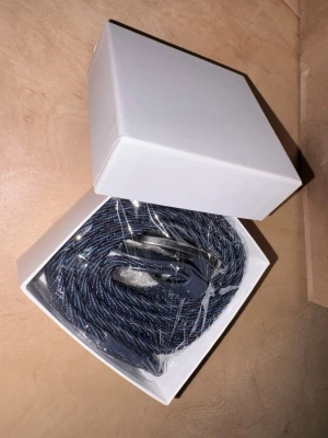 Blå flätad bälte med skinnspänne - Säljer ett snyggt blått flätat bälte med detaljer i konstläder och metallspänne. Bältet har en mix av mörkblå och ljusblå toner i det flätade bandet och ett stilrent spänne i silverfärg. Perfekt accessoar för att lyfta din outfit.