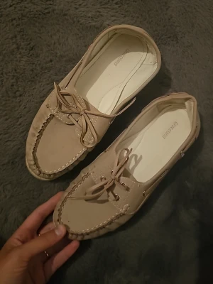 Beige seglarskor från Greenland - Säljer ett par klassiska beige seglarskor från Greenland. Skorna har snörning framtill, dekorativa sömmar och är tillverkade i mocka. Perfekta för dig som gillar en avslappnad men ändå stilren look.