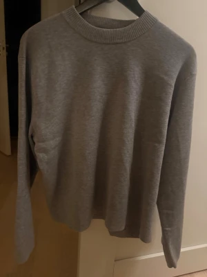 Grå basic tröja från H&M - Enkel och stilren grå tröja från H&M i storlek S. Tröjan har rund halsringning med ribbad kant och långa ärmar. Perfekt till lager på lager och funkar året runt. Materialet är mjukt och skönt, troligtvis bomull eller bomullsblandning.