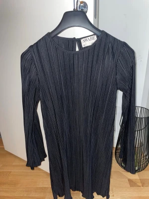 Svart plisserad klänning från AWARE - Säljer en svart plisserad klänning från AWARE med långärmad design och rund hals. Klänningen har en snygg plisserad struktur och är i ett mjukt, stretchigt material som ger en bekväm passform. Använd 1 gång.