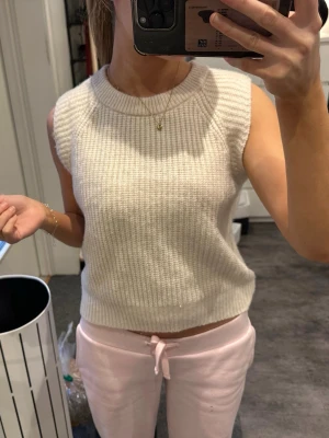 Stickad ärmlös topp i beige - Säljer en superfin stickad topp i beige med grov ribbad struktur. Modellen är ärmlös med rund halsringning och croppad passform. Perfekt att styla med både jeans och kjol för en chill look. Aldrig använt helt ny