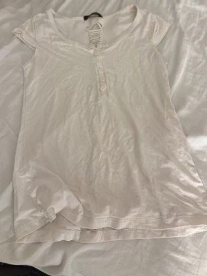 Vit topp med snörning från MNG Suit - Vit kortärmad topp från MNG Suit i mjuk bomull. Snygg snörningsdetalj både fram och längs ryggen samt knappar framtill. Perfekt för dig som gillar unika detaljer och en avslappnad stil.