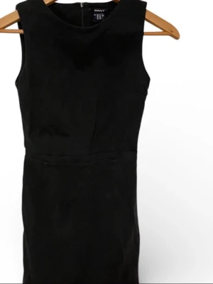 Svart ärmlös klänning från Gant - Klassisk svart ärmlös klänning från Gant med rund halsringning och diskret dragkedja i ryggen. Stilren och enkel design i ett strukturerat tyg som ger en snygg siluett. Perfekt att styla med accessoarer för en personlig touch.