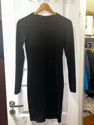 Svart ribbad klänning från Gina Tricot - Säljer en svart, ribbad klänning från Gina Tricot i storlek S. Klänningen är figurnära med lång ärm och rund halsringning. Enkel och stilren design som passar perfekt till många olika looks.