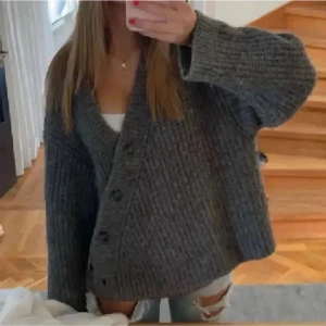 Stickad & other stories kofta - Mysig grå stickad kofta med v-ringning och stora knappar framtill. Koftan har en loose passform och långa ärmar, perfekt att slänga över ett linne eller t-shirt. Ribbstickade muddar och en chunky känsla gör den extra trendig. VÄLDIGT EFTERTRAKTAD!! TAR BUD!