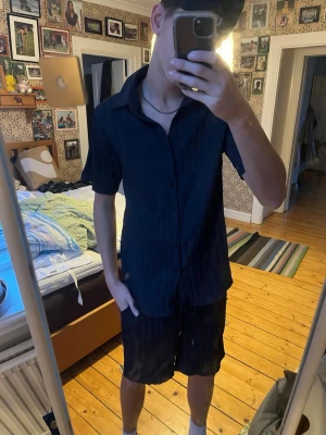 Mörkblå randiga shorts med snörning - Säljer ett par mörkblå shorts med vertikala ränder och elastisk midja med snörning. Shortsen har en loose passform och är tillverkade i ett mjukt, lätt material som passar perfekt till sommaren. Snygga att matcha med en enkel t-shirt eller skjorta.