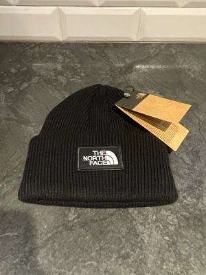Svart ribbad mössa från The North Face - Säljer nu denna nya oanvända svarta ribbstickade mössa från The North Face! Mössan är unisex och har en uppvikt kant för extra stilpoäng. Det är ONE SIZE så passar alla, Perfekt accessoar för kyliga dagar! Vid intresse bara att höra av sig. 