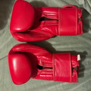 Röda Cleto Reyes boxningshandskar - Säljer ett par klassiska röda Cleto Reyes boxningshandskar i skinn. Handskarna har bred kardborrestängning vid handleden och svart innerfoder. Märket är tydligt broderat på ovansidan och mudden. Perfekta för dig som vill träna boxning med stil. Handskarna är andvända sparsamt för säck träning så små skavanker finns här o där men inget som på verkar handskarna !  Cleto reyes stämpeln och serienummer finns fråga i chatten så får ni se bilder  , nypris 3300kr