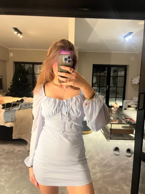 Ljusblå kort klänning med puffärmar - Supersöt ljusblå kort klänning med långa puffärmar och snörning framtill vid bysten. Klänningen har en figurnära passform och är tillverkad i ett mjukt, lätt material som ger en romantisk vibe. Perfekt för dig som vill sticka ut med en feminin och trendig look.