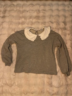 Grå tröja med volangkrage från Cubus - Supersöt grå tröja från Cubus i storlek M med långärmad passform och en stor vit volangkrage som ger en gullig och trendig look. Perfekt till både jeans och kjol för en chill men ändå stylish outfit.