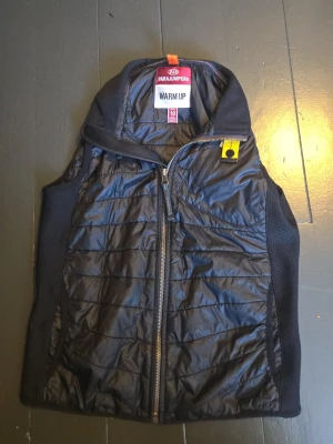 Svart dunväst från Parajumpers - Säljer en svart dunväst från Parajumpers med quiltad design och dragkedja framtill. Västen har en sportig look med meshpaneler på sidorna och en gul detalj vid kragen. Perfekt för lager-på-lager och riktigt snygg till höst och vinter.