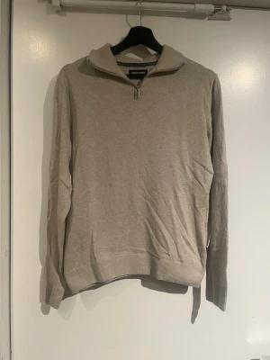 Jack & Jones - Säljer en stilren beige tröja från Jack & Jones med half zip-dragkedja i halsen. Tröjan har lång ärm, ribbade muddar och en mjuk känsla. Perfekt till jeans eller chinos för en clean look.