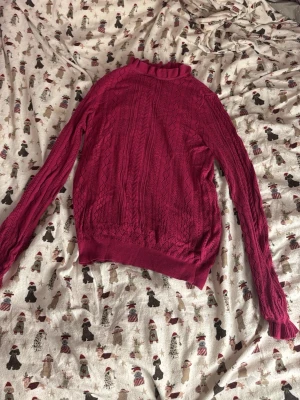 Mörkrosa stickad polotröja Vero Moda - Säljer en mörkrosa stickad polotröja från Vero Moda i storlek S. Tröjan har ett detaljerat hålmönster, volangkant vid hals och ärmslut samt lång ärm. Perfekt för dig som vill ha en mysig och snygg tröja till hösten eller vintern.