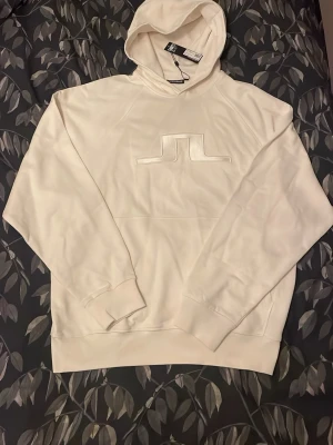 Vit J.Lindeberg hoodie - Schysst vit j.lindeberg hoodie som är väldigt snygg nu till vintern. Den har kvar sitt kvitto och är oanvänd, säljs pga för stor. Det är även populärt märke bland ungdomar, så passa på. Skriv för fler frågor!