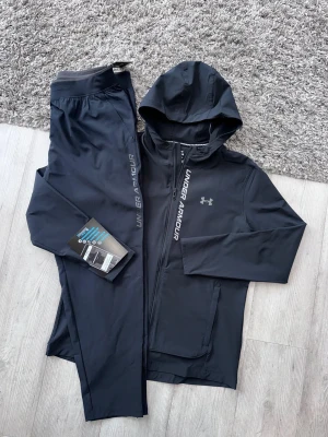UNDER ARMOUR STORM TRACKSUIT - UNDER ARMOUR STORM TRACKSUIT- svart och blå   Sitter riktigt snyggt på kroppen och materialet är stretchigt/bekvämt