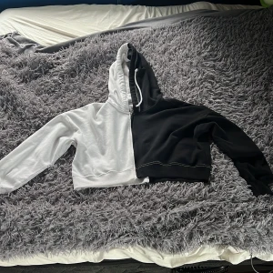 Svartvit hoodie från Hollister - Säljer en cool hoodie från Hollister i storlek M.  Tröjan är svart och vit, delad mitt på med dragkedja och snörning i huvan.  Croppad modell med långa ärmar och mjukt bomullsmaterial.  Perfekt för dig som gillar streetstyle och kontraster.