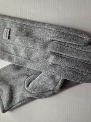 Gråa eleganta handskar  - Bilderna visar ett par gråa handskar i mjukt material. Handskarna har en enkel design och en liten etikett med texten 'Fashion Gloves'.