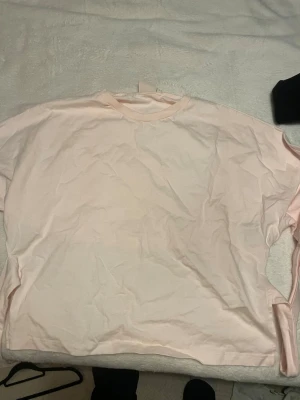 Ljusrosa långärmad t-shirt med knyte bak - Säljer en enkel och stilren ljusrosa långärmad t-shirt med rund hals. T-shirten är tillverkad i mjuk bomull och har en avslappnad passform som gör den skön att bära. Perfekt för dig som gillar minimalistisk stil och mjuka färger.