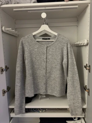 Grå stickad kofta  - Mysig grå stickad kofta från lager 157 med rund hals och knappar hela vägen framtill. Koftan har långärmad passform.