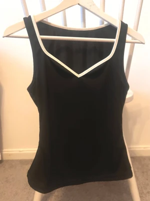 Svart linnetopp med vit kant - Snygg svart linnetopp med vit kant runt halsringningen. Toppen har en v-ringad design och är ärmlös, vilket gör den perfekt för varma dagar. Materialet känns mjukt och följsamt mot kroppen. Enkel och stilren modell som är lätt att matcha med olika outfits.