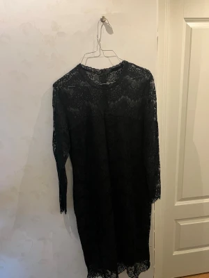 Svart spetsklänning från KappAhl - Supersnygg svart spetsklänning från KappAhl i storlek 44. Klänningen har långärmade ärmar, rund hals och vackra spetsdetaljer över hela plagget. Den stängs med en diskret dragkedja i ryggen och har en klassisk, rak siluett som ger en elegant look. Klänningen är endast använda 1 gång✨