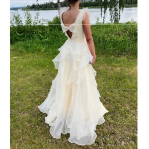 Balklänning - Intressekoll på min balklänning med v-ringning och volangdetaljer. Klänningen har ärmlös design, öppen rygg med rosettdetalj. Rosetten går även att ta bort om det önskas. Skicket är nästintill nytt, endast använd en gång.  Storleken är ungefär mellan 36-38, vid intresse kan måtten kollas upp! Klänningen är köpt från usa med nypris på ca 9000kr. Mitt pris är 4000kr, priset kan diskuteras!🥰