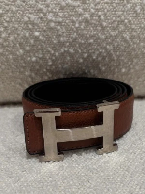  H-bälte - Säljer ett stilrent H-bälte i brunt och svart skinn med ett ikoniskt H-spänne i silverfärgad metall. Bältet har en klassisk design och passar perfekt till jeans eller kostymbyxor. Märket är ingraverat på spännet för extra lyxkänsla. Kom dm för eventuella frågor 🧐pris kan diskuteras 💯😊