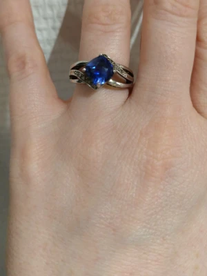 Silversring med blå safir och diamanter - Säljer en snygg ring i äkta silver (925) med en stor blå, facetterad lab skapad safir i centrum. Ringen har en cool design med snirkliga detaljer på sidorna och små glittrande äkta diamanter längs bandet. Perfekt för dig som gillar unika smycken med lite extra bling. 17,5 mm i inner diameter 