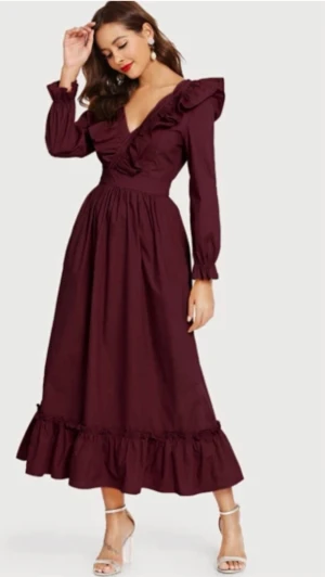Surplice V Neck Ruffle Dress - Säljer en vinröd långklänning med v-ringning, långa ärmar och volangdetaljer vid axlar och nederkant. Klänningen har en markerad midja och är tillverkad i ett mjukt bomullsliknande material. 