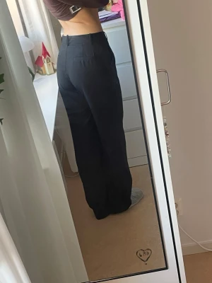 Svarta kostymbyxor från NLY Trend - Säljer ett par svarta kostymbyxor från NLY Trend i storlek 36. Byxorna har hög midja, raka ben och en loose fit som ger en chill vibe. Klassisk look med hällor för bälte och diskreta bakfickor. Perfekta till en snygg topp eller oversized skjorta.