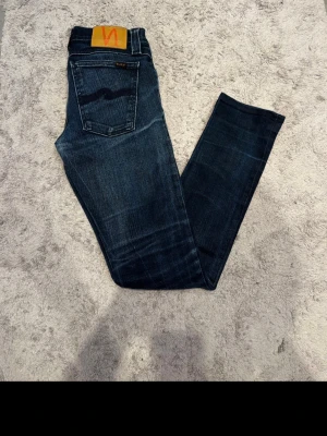 Nudie Jeans Tight Long John  - Snygga mörkblå jeans från Nudie Jeans, modellen Tight Long John. De har klassisk femficksdesign, smal passform och är tillverkade i bomull. Bakfickorna har Nudie Jeans signaturbroderi och ett läderpatch med logga.