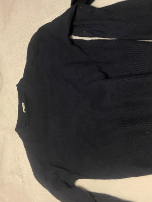 Mörkblå stickad tröja - Mysig mörkblå stickad tröja med rund hals och långa ärmar. Tröjan har ribbade detaljer vid halsringning, ärmslut och nederkant. Perfekt för kyliga dagar och enkel att matcha med jeans eller kjol.