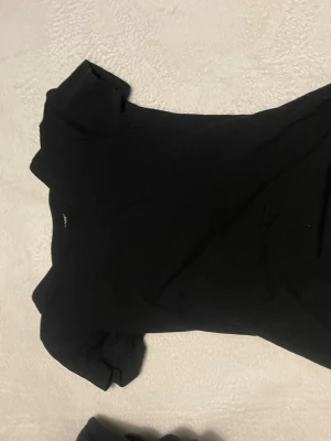 Svart basic t-shirt  - En svart, enkel t-shirt från  med rund hals och korta ärmar. Modellen är klassisk och passar perfekt till jeans eller shorts. Materialet är mjukt och skönt bomull som känns bekvämt mot huden. Perfekt för dig som gillar stilrena och tidlösa plagg.