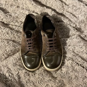 Bruna sneakers från Lanvin i mocka - Säljer ett par bruna sneakers från Lanvin med ovandel i mocka och lackad tå. Skorna har bruna snören, vit sula och rund tå. Snygg kontrast mellan material och en stilren design som passar till många outfits. Jag har köpt nya snören till de för de andra försvann och det finns såklart små skavanker med skorna därav priset, kan även sänka vid snabb affär🤗🤗