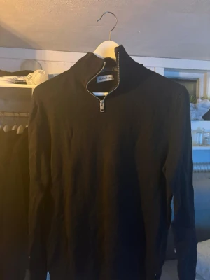 Svart half zip tröja Jack & Jones - Svart långärmad tröja från Jack & Jones i storlek S. Tröjan har en hög krage med half zip-dragkedja och är tillverkad i mjukt stickat material. Perfekt för dig som gillar stilrena och enkla plagg med lite edge.
