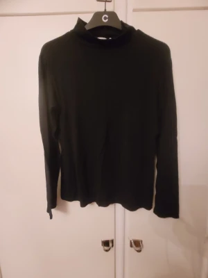 Svart polotopp från Armand Thiery - Svart långärmad polotopp från Armand Thiery. Enkel och stilren design med hög krage och mjukt material som känns skönt mot huden. Perfekt att matcha med jeans eller kjol för en clean look.