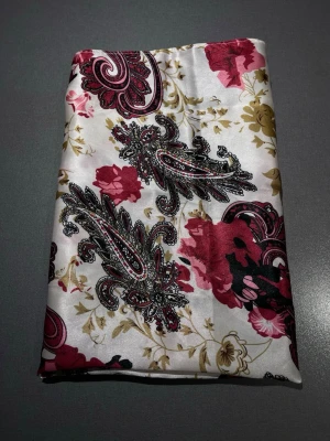 Blommig paisley mönstrad scarf - Scarf i imitationssiden/satib med blommigt och paisley mönster i rött, svart, beige och guld på vit botten. Scarfen har en mjuk och glansig yta som känns lyxig och sticker ut med sitt detaljerade tryck. Perfekt att knyta runt halsen till en tröja eller runt handväskan för en fin detalj! Mått: ca 50x50cm, något skevt skuren. Mycket bra skick, som ny! Säljs på flera sidor, först till kvarn. 