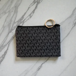 Svart MK plånbok med mönster - Snygg plånbok från Michael Kors i svart med grått MK-mönster över hela ytan. Plånboken har en praktisk dragkedja och en guldfärgad ring för att enkelt fästa i nycklar eller väska. Perfekt för kort och småsaker.