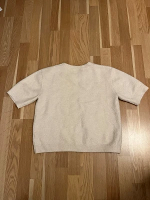 Beige stickad tröja från Kappahl - Säljer en beige stickad tröja från Kappahl i storlek 158/164. Tröjan har korta ärmar, rund hals och ribbade muddar vid ärmslut och nederkant. Perfekt för dig som gillar enkel och stilren design.