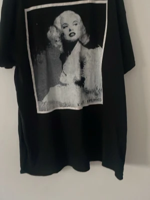 L’arte t-shirt - Cool svart t-shirt från L'ANE med stort grafiskt tryck i gråskala framtill och texten 'EST. 2023' längst ner. Oversized passform och korta ärmar, perfekt för en avslappnad streetstyle-look.