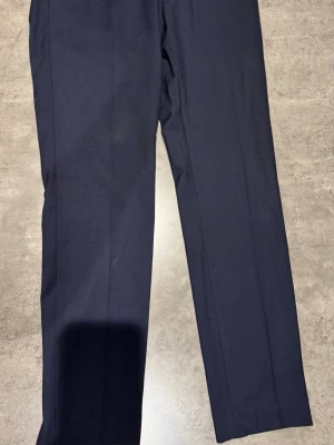 Mörkblå kostymbyxor Riley slim fit - Snygga mörkblå kostymbyxor från Riley i slim fit-modell. Tillverkade i en mix av polyester, viskos och elastan för skön stretch och bra passform. Klassisk rak design med pressveck och diskreta fickor.