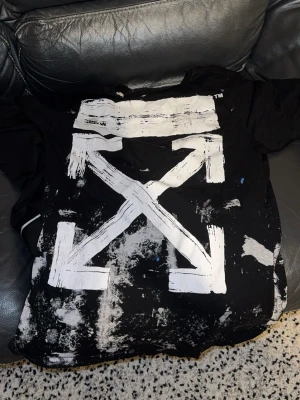 Svart Off-White t-shirt med tryck - Svart t-shirt från Off-White med stort vitt grafiskt tryck på ryggen och färgstänk i blått, rosa och grönt på framsidan. T-shirten har korta ärmar och rund hals. Materialet är mjuk bomull och designen är riktigt street med konstnärlig vibe.