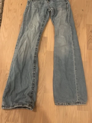 Blå bootcut jeans från Gina Tricot - Snygga ljusblå jeans från Gina Tricot i storlek 140. Modellen har bootcut-ben, klassiska fem fickor och dubbla knappar i midjan. Jeansen är tillverkade i jeansmaterial med slitna detaljer och kontrastsömmar.