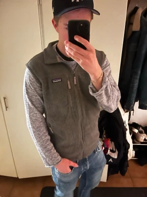 Grå fleeceväst från Patagonia Synchilla - Säljer en grå fleeceväst från Patagonia Synchilla i storlek L men den passar M. Västen har dragkedja framtill, hög krage och flera praktiska fickor med dragkedja. Tillverkad av 100% återvunnen polyester, perfekt för lager-på-lager och chill vardagsstil.