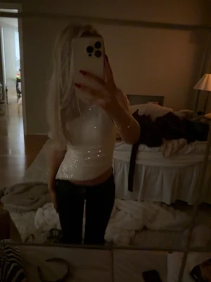 Vit glittrig croppad topp - Säljer en vit glittrig croppad topp med ärmlös design. Toppen har en snygg, figurnära passform och är perfekt för att sticka ut. Materialet är syntet och har en skimrande finish som fångar ljuset. Passar dig som gillar att glänsa och vill ha något extra till din outfit.